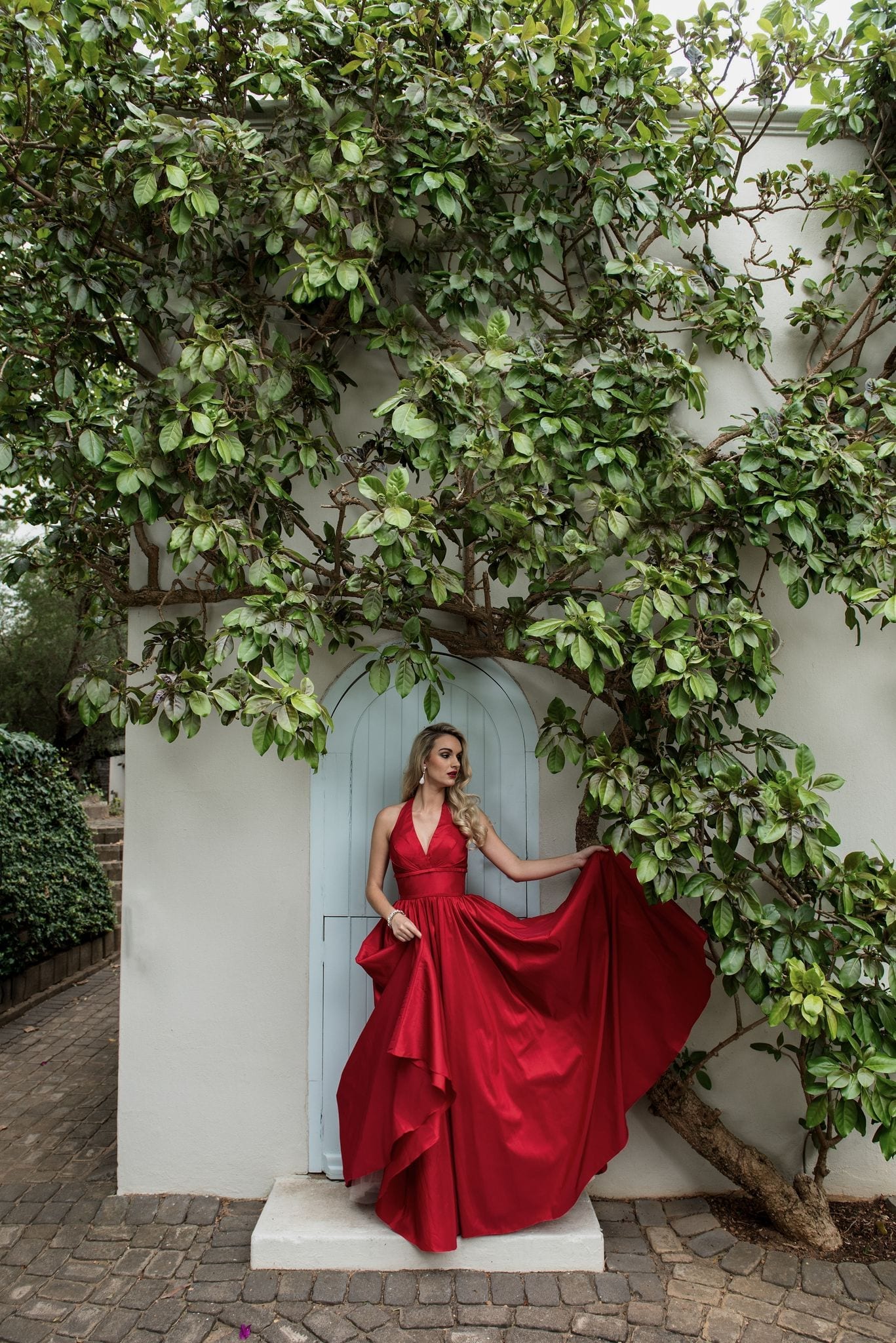Fashion photography - Woman in flowing red dress by vintage blue door with climbing vines